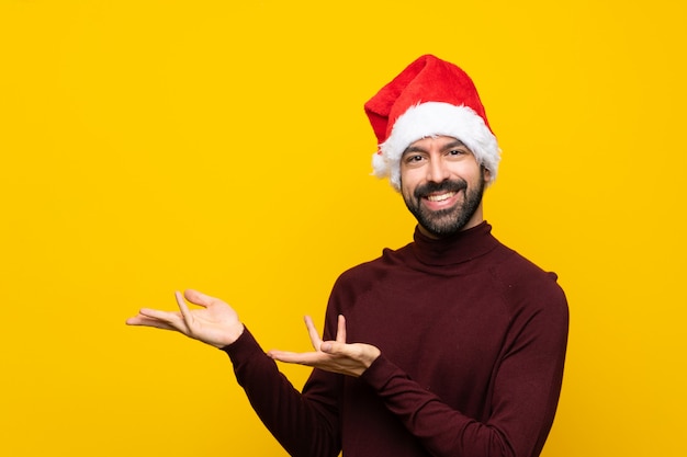 来て招待する側に手を拡張する孤立した黄色の壁の上のクリスマス帽子の男