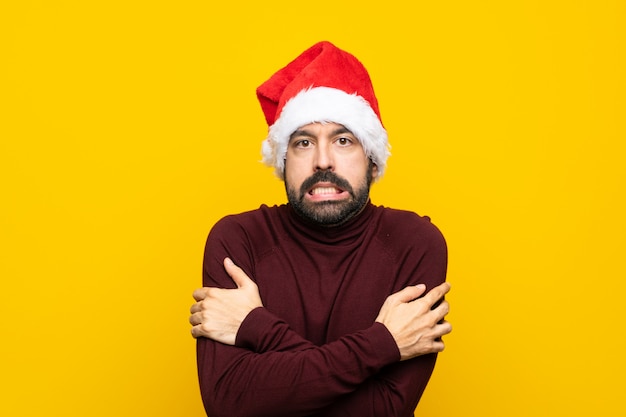 Man with christmas hat over isolated yellow wall freezing