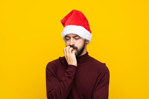 Man with christmas hat over isolated yellow wall having doubts