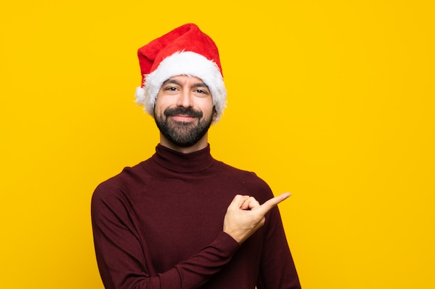 製品を提示する側を指している孤立した黄色の壁の上のクリスマス帽子の男