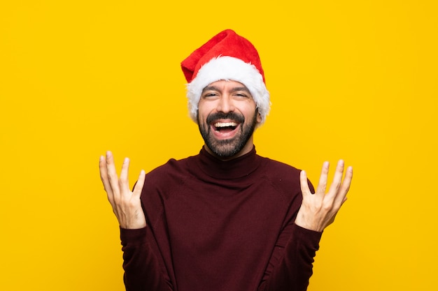 Man with christmas hat over isolated yellow wall smiling a lot