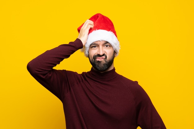 Человек с рождественской шляпой над изолированной желтой стеной с выражением разочарования и непонимания