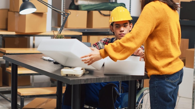 Man with chronic disability using laptop in warehouse, checking stock of merchandise for logistics and management. Young employee working in disability friendly space, supply chain.