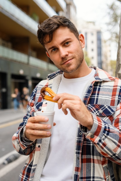 カップにチュロスとホットチョコレートを持つ男