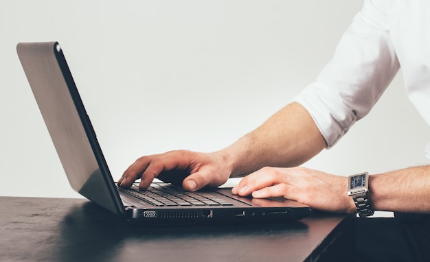 Man with clock on his hand works on the laptop at the table in the office. He is busy with the task