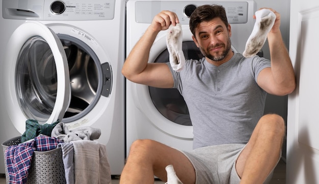 Man with clothes near washing machine handsome man sits in front of washing machine loads washer on