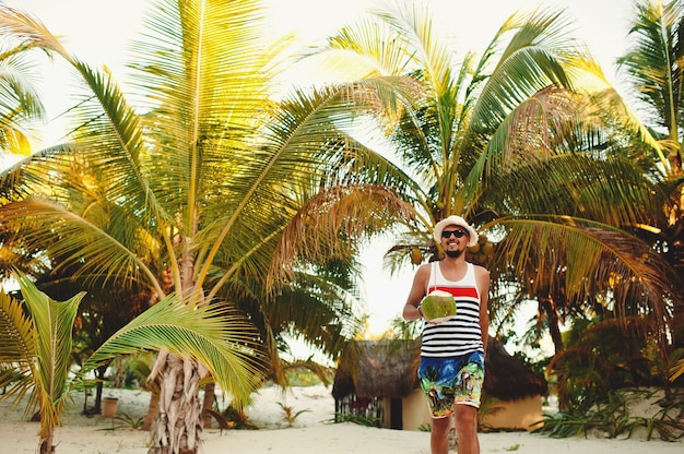 Man with coconut walking on the tropical beach on sunny day during vacation