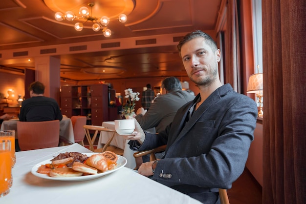 高級ホテルのダイニングテーブルに座ってコーヒーと朝食を持つ男性