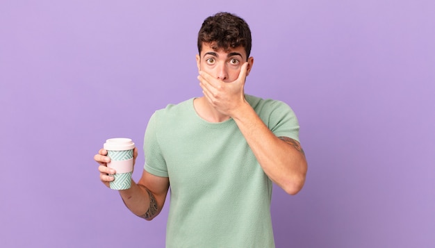 Man with coffee covering mouth with hands with a shocked, surprised expression, keeping a secret or saying oops