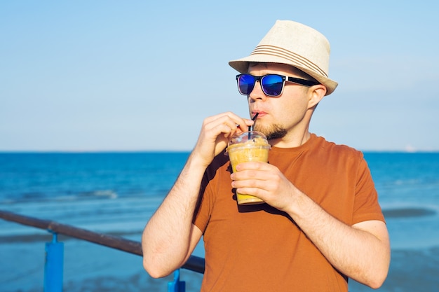 自由時間の休暇を楽しんで自由に海の近くでコーヒーフラッペを持つ男。
