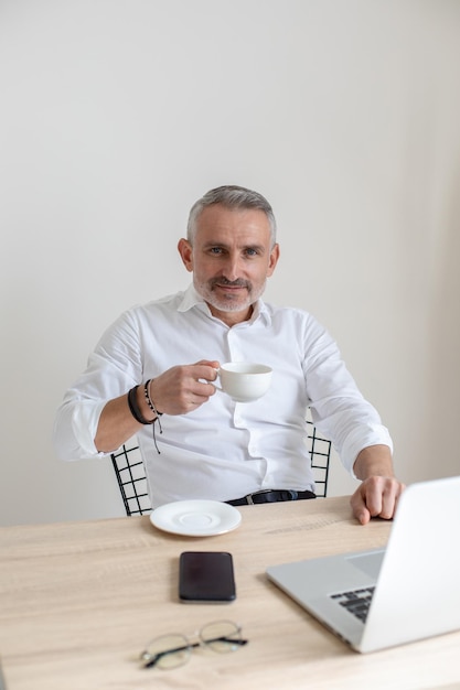 Uomo con caffè che guarda l'obbiettivo sul posto di lavoro