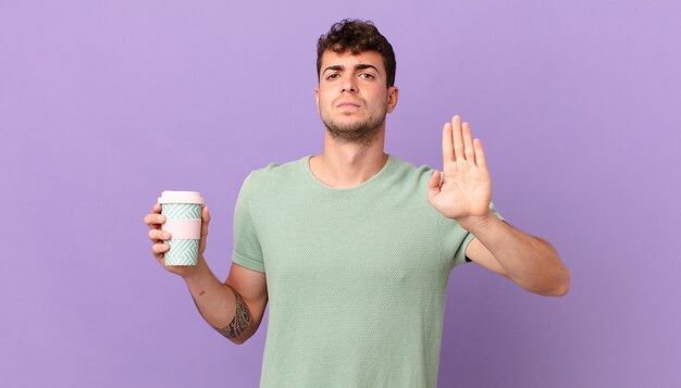 Man with coffee looking serious, stern, displeased and angry showing open palm making stop gesture