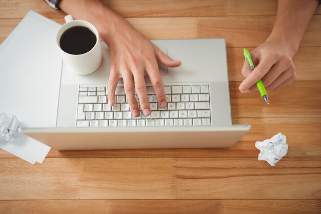 Photo man with coffee and pen working on laptop at desk in office