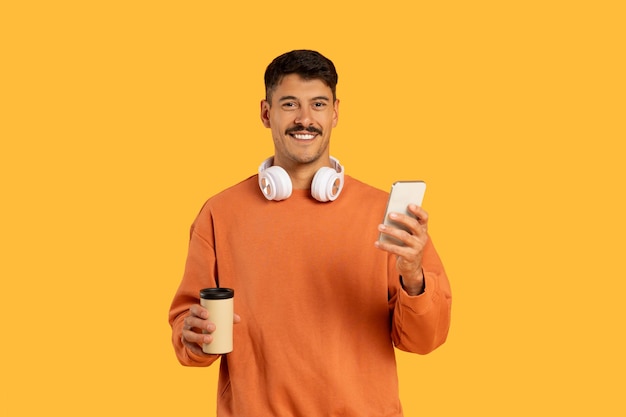 コーヒーとスマートフォンをつけた男性がヘッドフォンをかぶっている