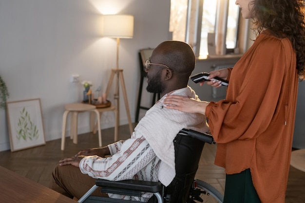 Мужчина с инвалидностью стрижет волосы электрическим триммером, который держит опекун