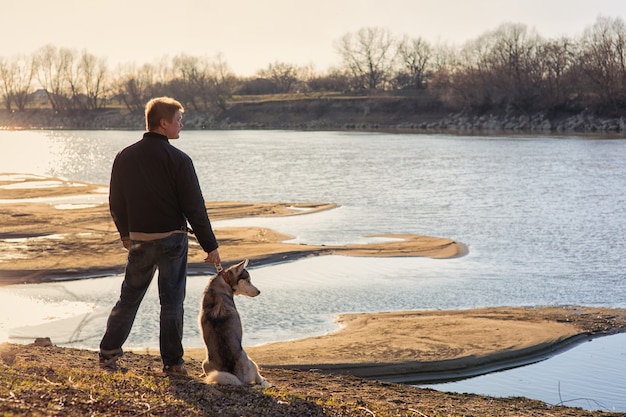 Man with a dog on the bank of the river at sunset