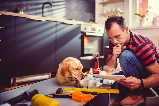 キッチンキャビネットを構築しながら青写真をチェックする犬を持つ男