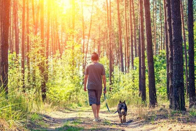 ひもにつないで犬を連れた男が森の未舗装の道路を歩く