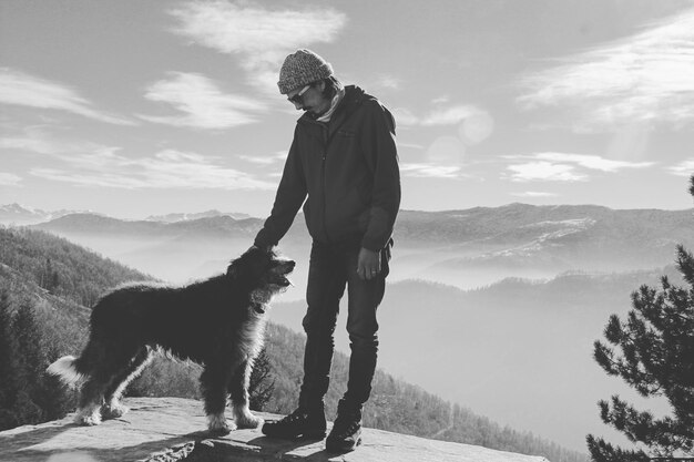 空に向かって山の上に立っている犬を持つ男