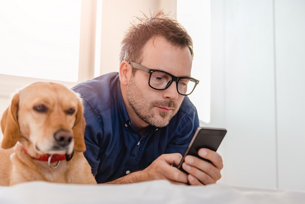 ベッドでスマートフォンを使用して犬を持つ男