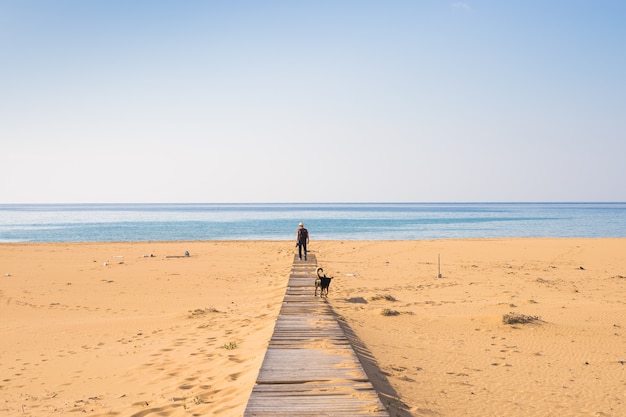 Man with dog walking on the tropical beach.