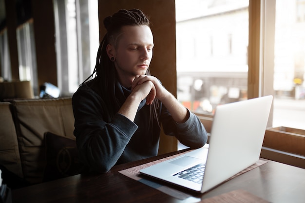 Uomo con il dreadlock in caffè con il computer portatile.