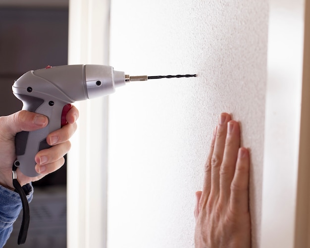 Uomo con trapano sul muro facendo buco