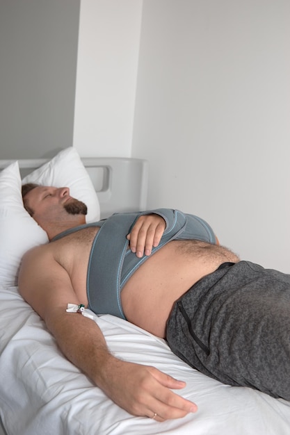 Фото Мужчина с катетером-капельницей лежит на кровати в больничной палате. перелом плеча эластичным бинтом. чрезвычайное происшествие