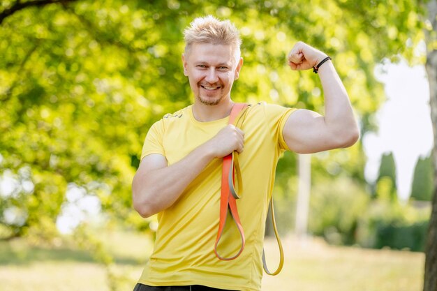 Man with elastic rubber band showing muscles outdoors after arm workout guy with sport equipment