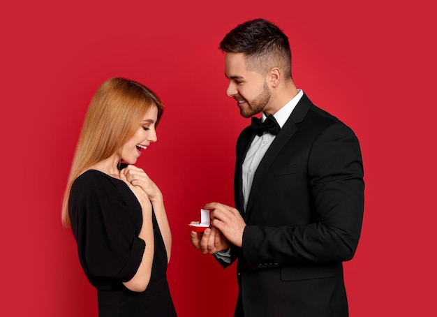 Мужчина с обручальным кольцом делает предложение руки и сердца девушке на красном фоне