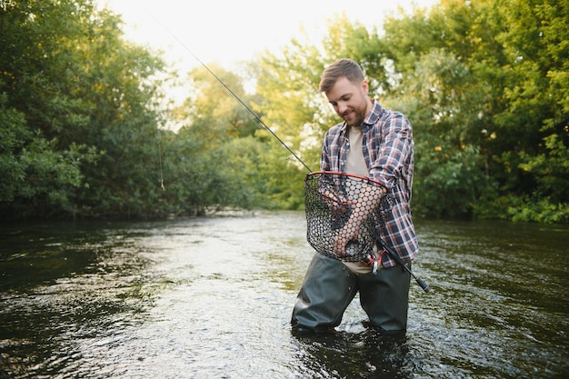 Man with fishing rod fisherman men in river water outdoor Catching trout fish in net Summer fishing hobby