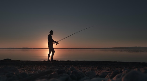 A man with a fishing rod on the shore of a picturesque lake in the early morning