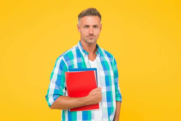 Man with folder yellow background. Businessman hold book for notes. guy has notepad for writing. handsome school or university teacher. adult man student holding notebooks. Inspired to work hard.