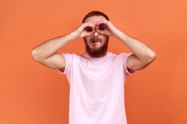 Man with funny face looking through fingers shaped like binoculars and expressing positive