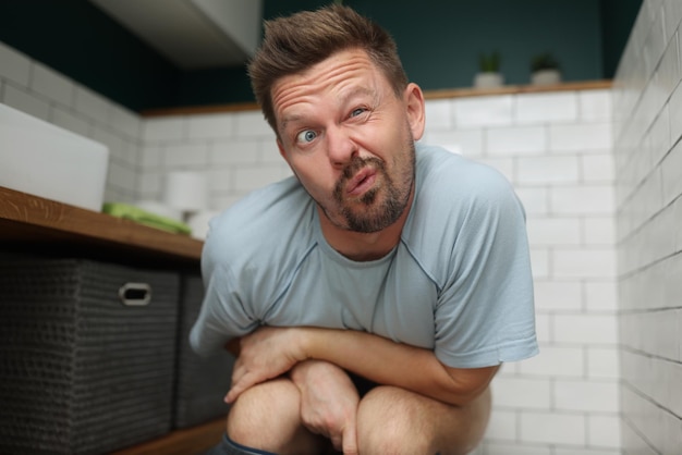 Man with funny facial expression on toilet seat fulfill natural need