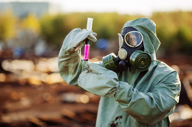 写真 防毒マスクと緑の軍服を着た男が化学災害後に樽を探検