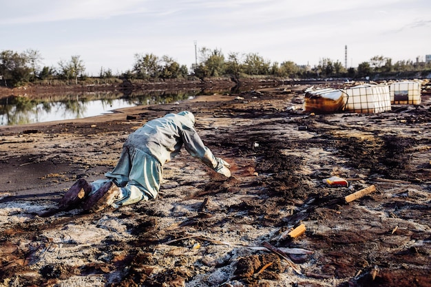 Фото Мужчина в противогазе и зеленой военной одежде исследует бочки после химической катастрофы
