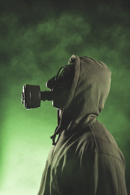 Man with gas mask on green background with smoke