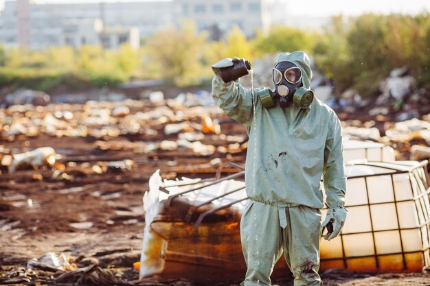 Man with gas mask and green military clothes explores barrels after chemical disaster