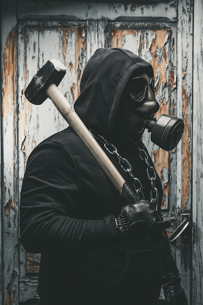 Foto uomo con la maschera antigas e un martello nella sala macchine. concetto di pericolo nucleare, biologico e chimico.