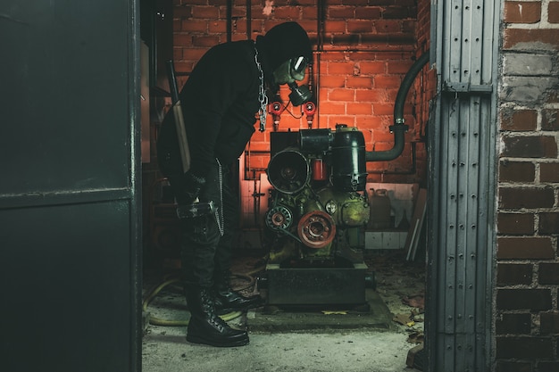 Man with gas mask and a hammer in machine room.