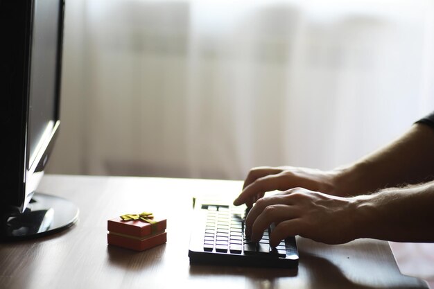 A man with a gift in his hand sits in front of the monitor\
screen order a gift for home and office