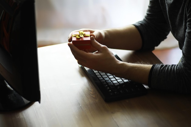 A man with a gift in his hand sits in front of the monitor\
screen order a gift for home and office