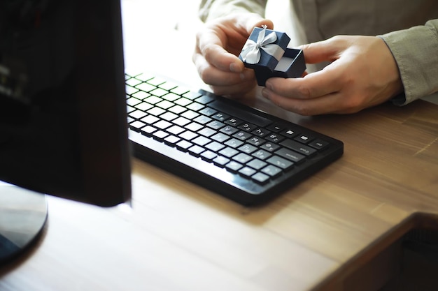 A man with a gift in his hand sits in front of the monitor\
screen order a gift for home and office