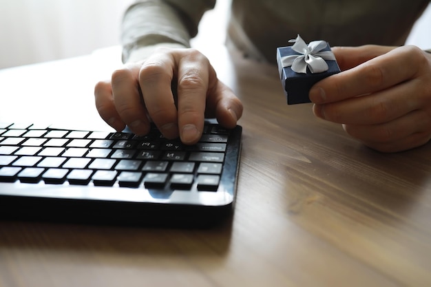 A man with a gift in his hand sits in front of the monitor\
screen order a gift for home and office