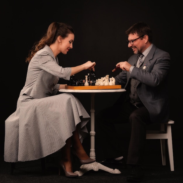 女の子と男はチェスをし、暗い背景でパイプを吸う