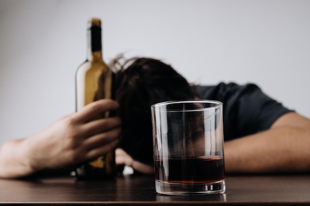 Man with glass and bottle of whiskey lying or sleeping on table Alcohol addiction concept