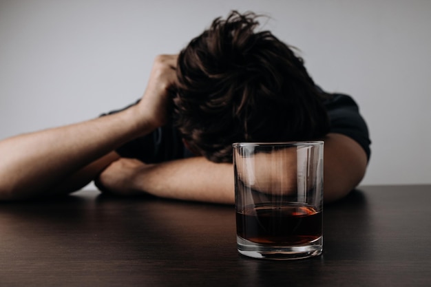 Man with glass of whiskey lying or sleeping on table Addiction concept