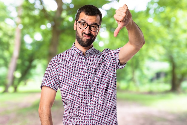 Man with glasses doing bad signal on unfocused background