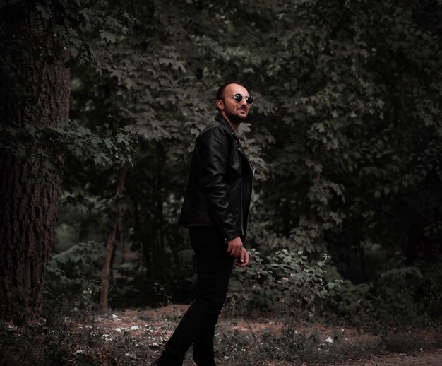 A man with glasses and a leather jacket makes a step against the background of the forest